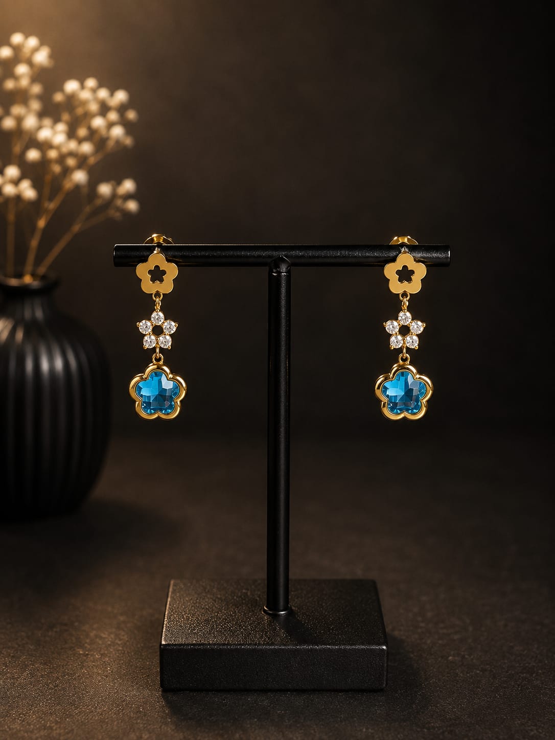 Boucles d'oreilles pendantes dorées fleurs cristal bleu - vue rapprochée sur présentoir noir