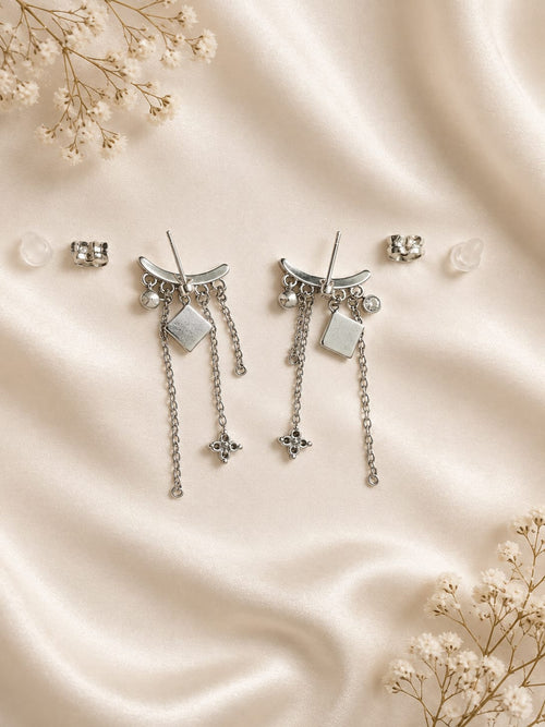Boucles d'oreilles pendantes argentées lune étoiles strass - vue à plat sur satin crème